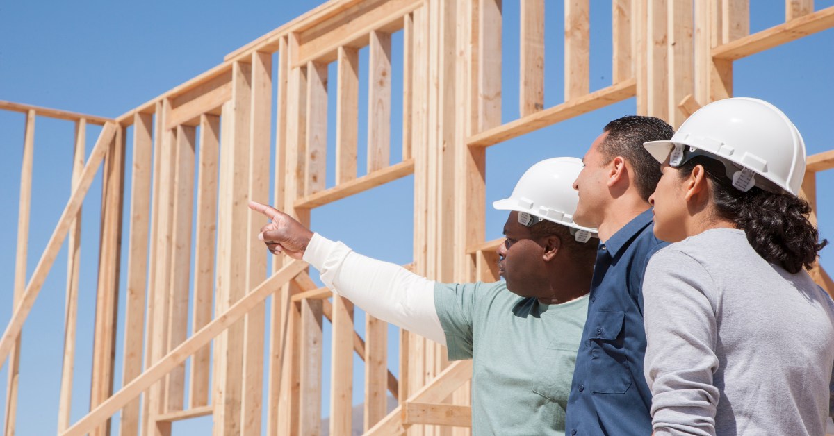 Builders in hard hats reviewing a wood-frame house under construction