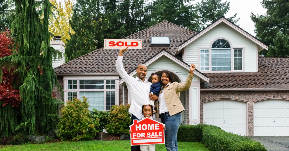 Family celebrating in front of their new home with SOLD and Home For Sale signs