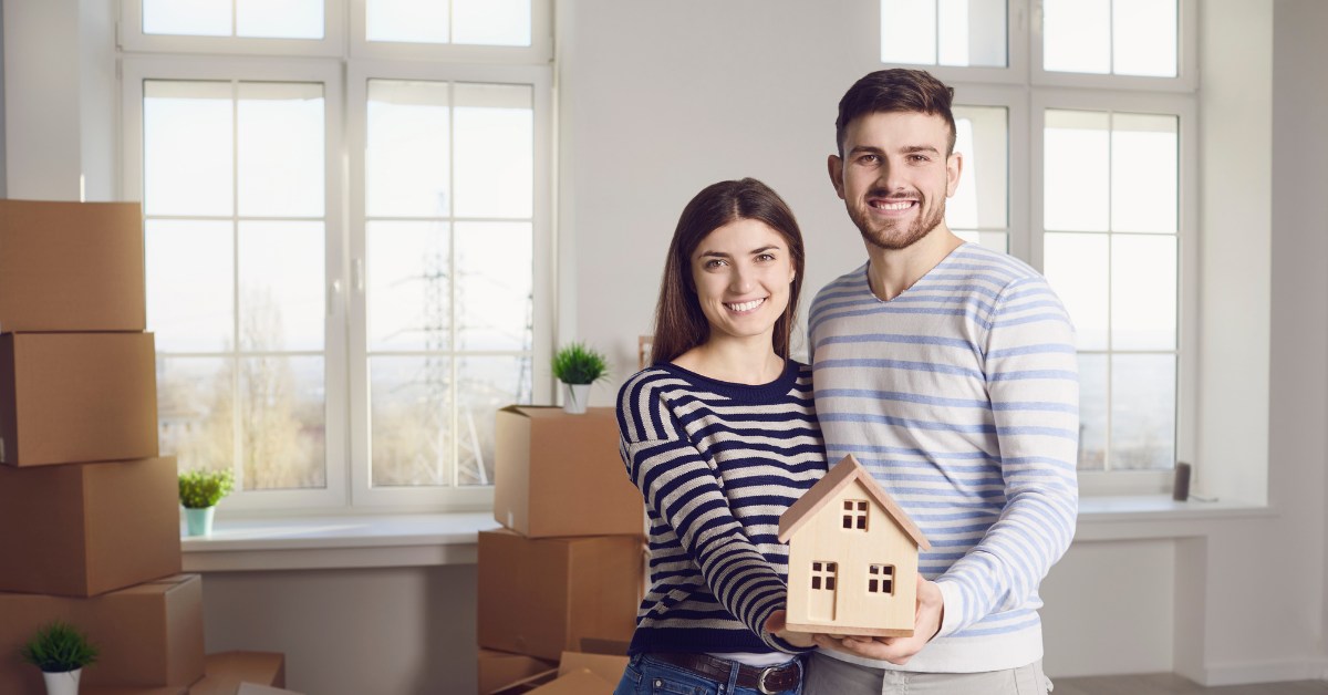 Couple holding a small model house in their new home surrounded by moving boxes