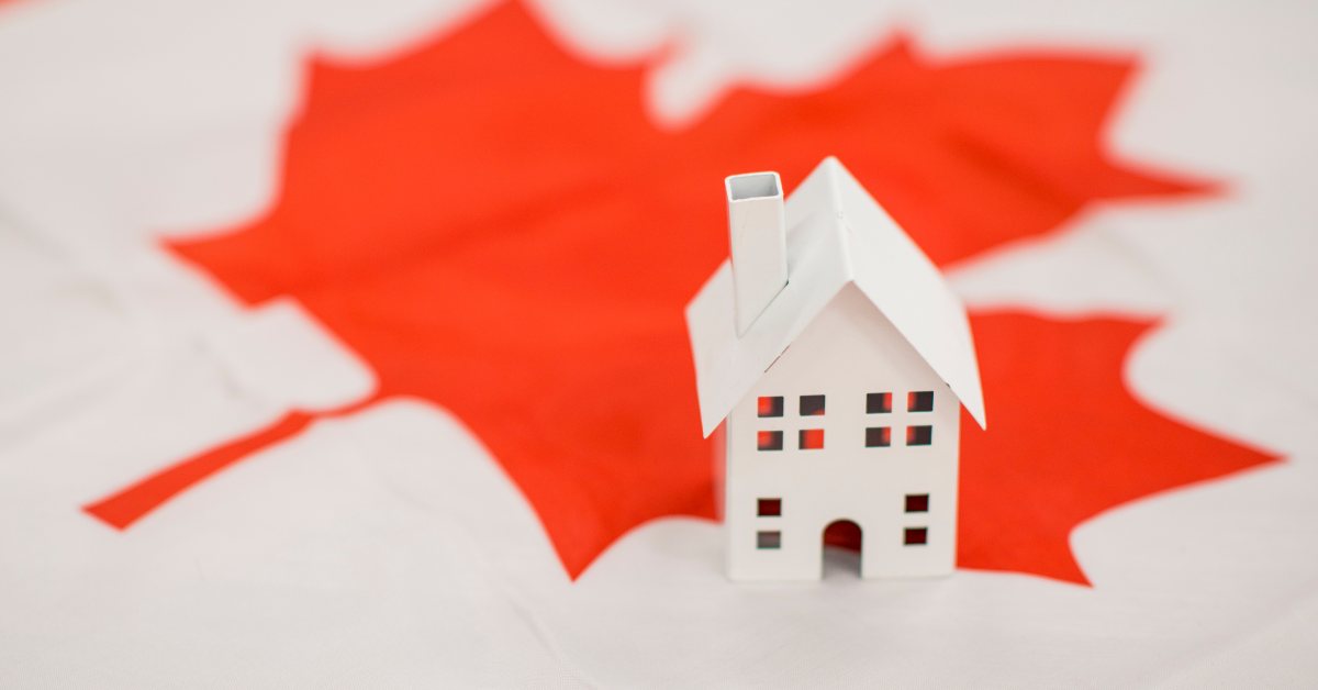 Miniature house resting on a red maple leaf